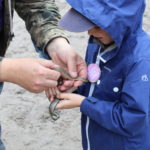 Member of ARC team helping a small child hold a smooth snake.