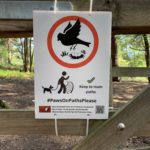 Photo of one of our "Paws On Paths Please" signs. A black and white illustration of a bird flying up from its nest on the ground. Asks everyone to "Keep to main paths".