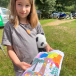 Photo of a small child who holds out a colourful painting of the forest.