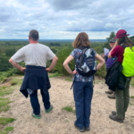 Photo of people standing at a view point. A man is looking out across the heathland and into the distance.