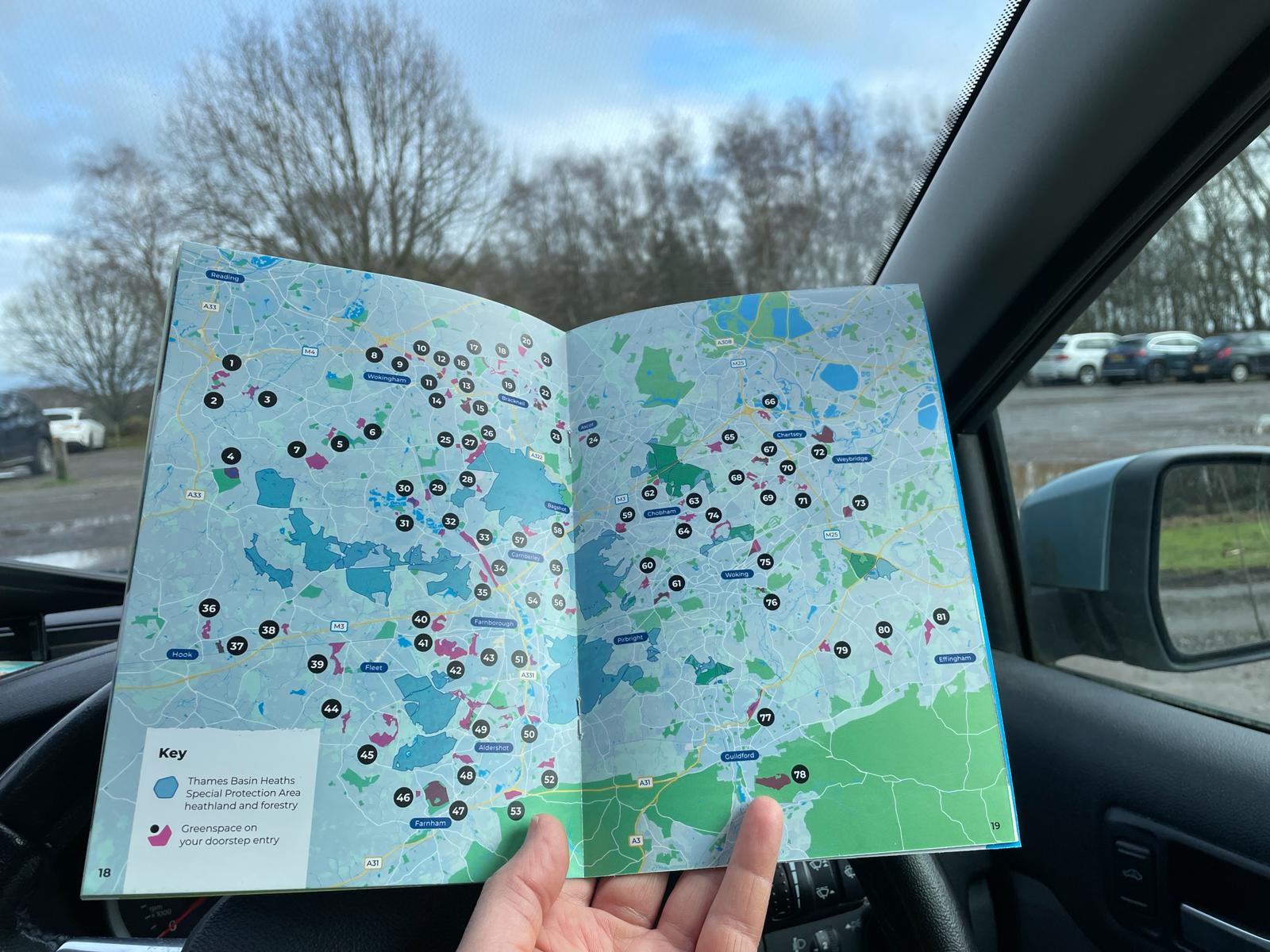 A hand holding an open booklet showing a map of heaths and numbered alternative greenspace walks