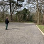 A man walks across a generously sized surfaced car park.