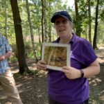 Photo of a lady in a purple t-shirt holding up a photo of a Nightjar, a bird that nests on the ground.