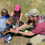 Photo of Education officer Michael kneeling down with a mum and her two children, they're looking closely at butterflies.