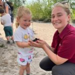 Photo of a little girl having her experience of holding a Slow Worm. She is being helped by a responsible adult.