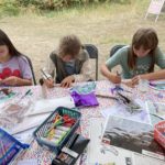 3 children sat at a table doing arts and crafts.