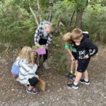 A group of children inspect a sign in a heathland landscape.