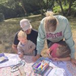 A family sat at a table getting stuck into arts and crafts activities against a forest background.