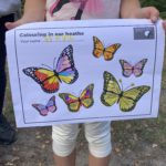 A child holding an A4 page decorated with brightly coloured butterfly drawings.