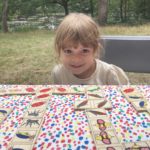A child sat at a table playing a game against a green landscape.