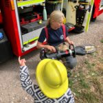 Photo of a female firefighter showing equipment from a fire engine to a young child