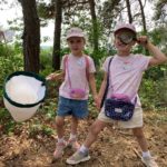 Photo of two young girls in pink posing with a butterfly net and magniflying glass