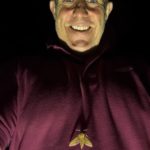 Photo of a man standing in the dark with a light highlighting a moth that has landed on him