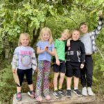 Photo of group of young children lined up and posing with a backdrop of green trees