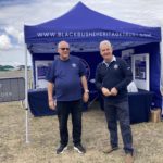 Photo of two men standing in front of a blue Blackbushe Hertitage Trust gazebo