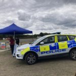 A police vehicle against a backdrop of a gazebo with two figures at the Heath Week 2025 event at Blackbushe Airport.