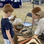 Photo of a female living history character looking at bronze age tools with a child