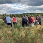 A group of people standing in heathland listening to a guided history tour.