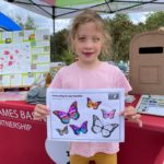 A child holding an A4 page decorated with bright butterflies against a backdrop of Thames Basin Heaths Partnership pop-up gazebo.