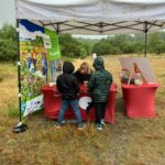 Photo of a warden sat at a table under a gazebo talking to two children about heathland