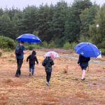Photo of a family leaving a rainy heath with large blue umbrellas