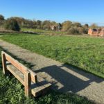 Photo of a green meadow in autumn with wooden bench, gravel path and houses in the distance