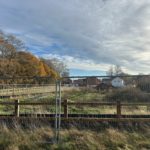 Photo of a housing estate under development with large metal barriers preventing access from a grassy area